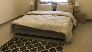 A modern bedroom with a large bed, two bedside tables, a patterned rug, and a window with curtains. - Muhanna Chalets (Al Khiran)