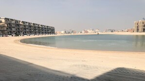 A sandy beach with a row of multi-story buildings in the background. - Muhanna Chalets (Al Khiran)