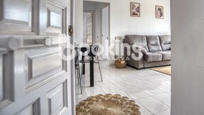 A modern living room with a grey sofa, a dining table with chairs, and a wicker rug on the floor.