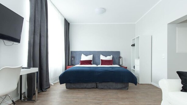 A modern hotel room with a large bed, a desk, and a TV mounted on the wall. - Chillinghouse 11 (Siegburg)