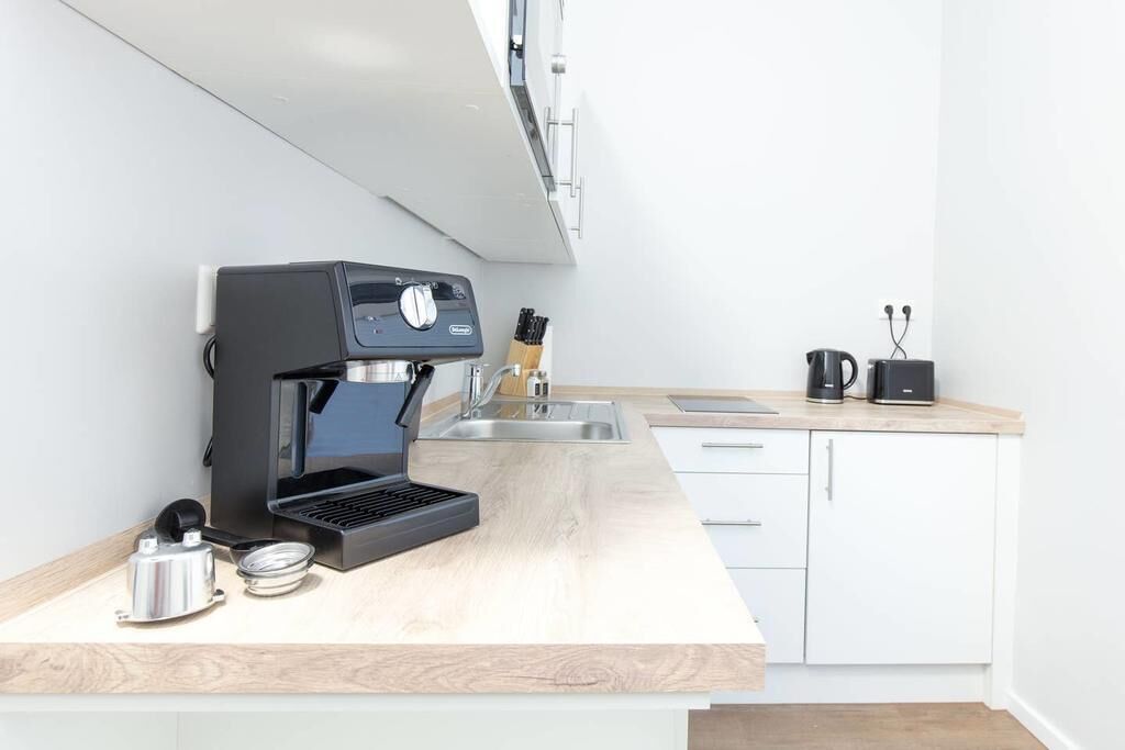A modern kitchen with a built-in espresso machine, a kettle, and a coffee maker on the countertop.