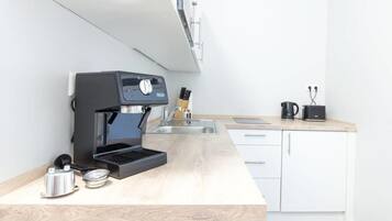 A modern kitchen with a built-in espresso machine, a kettle, and a coffee maker on the countertop.