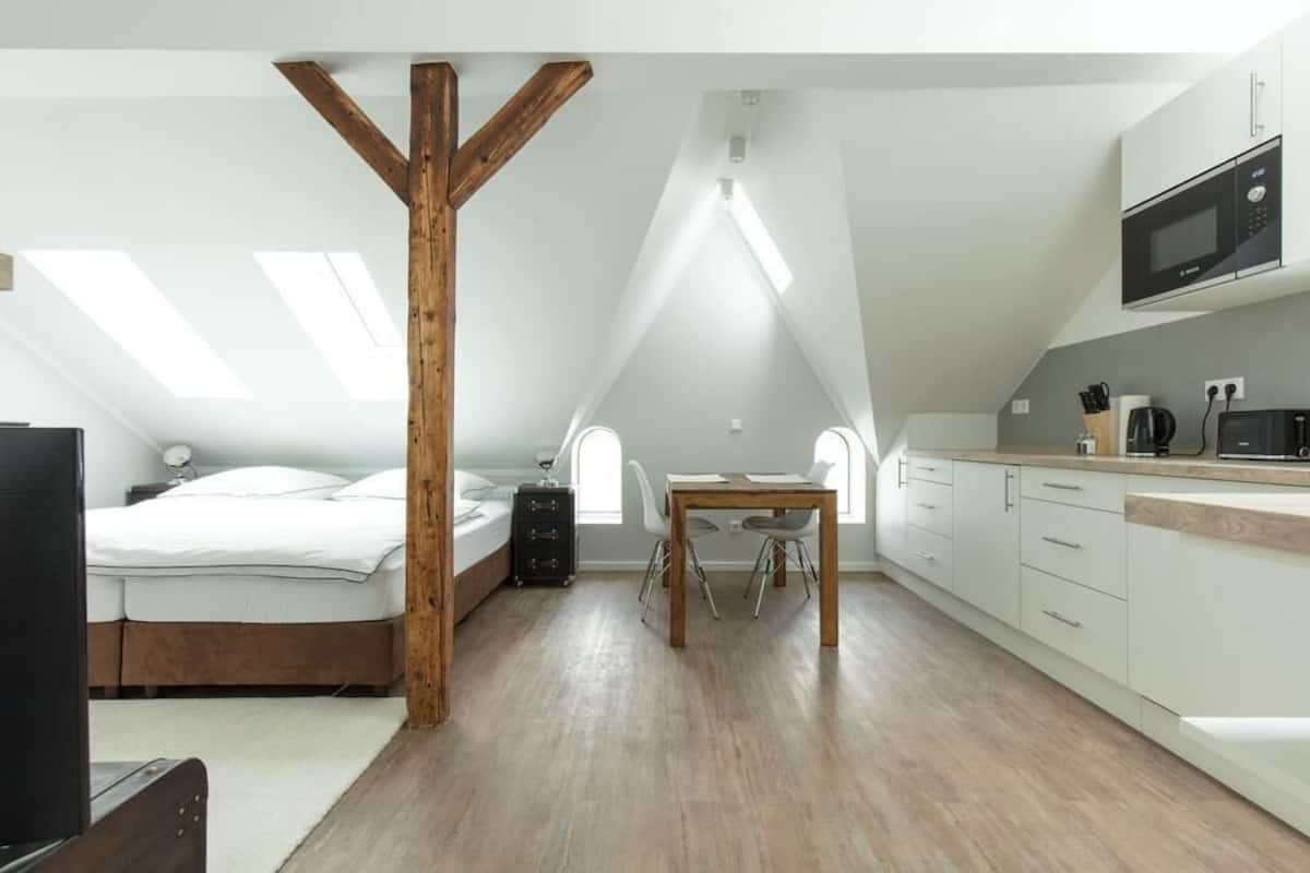 Une chambre de style loft moderne avec un plafond en poutres apparentes, un lit, un bureau et un coin cuisine.