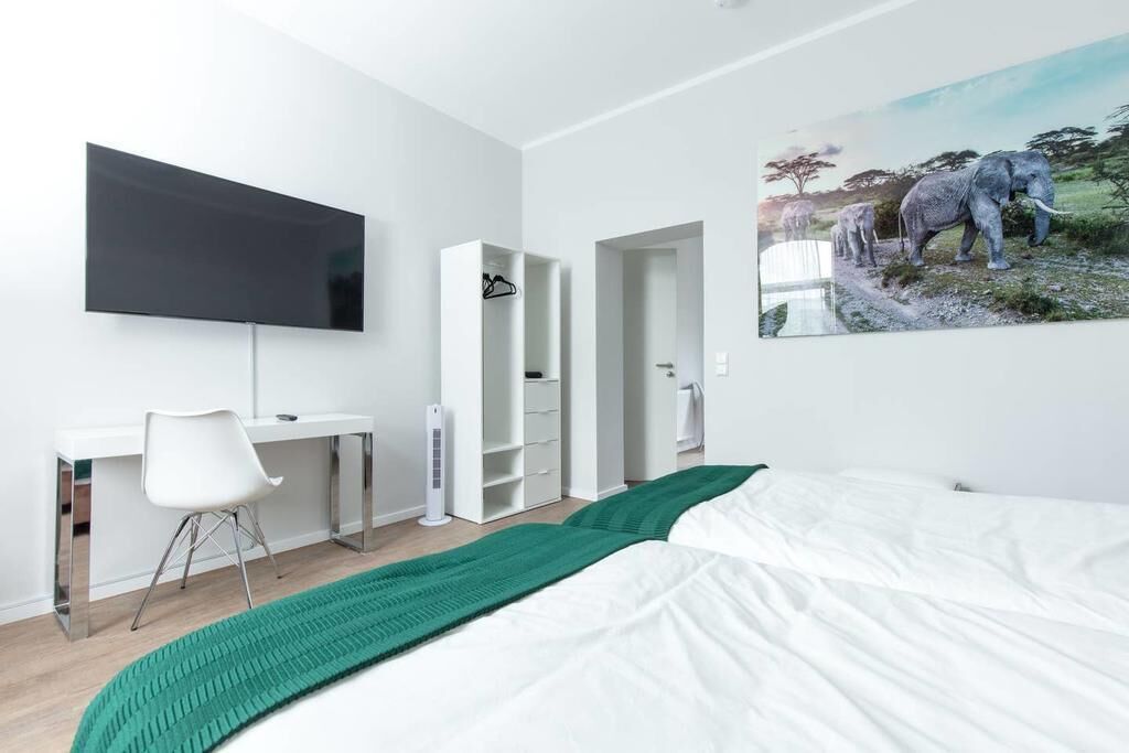 Un dormitorio moderno con cama, escritorio, silla, televisor y un cuadro de elefantes.