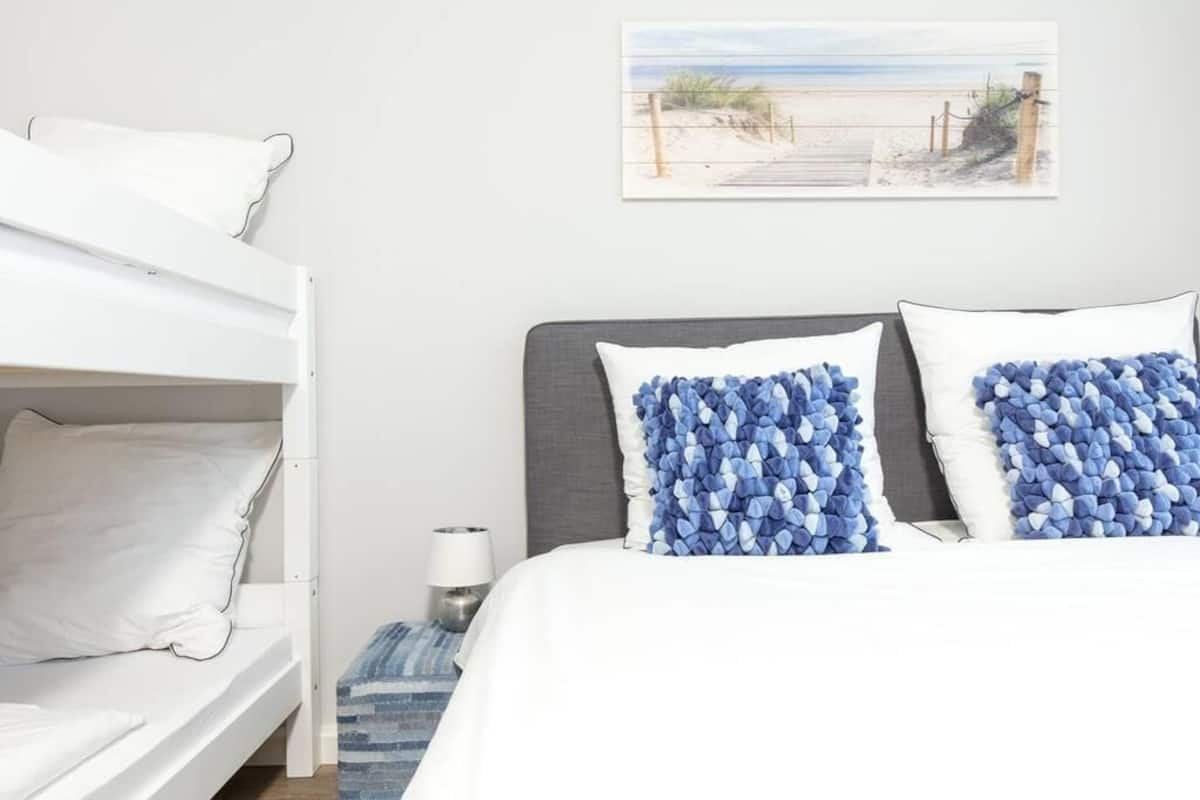 Une chambre avec un lit superposé, un lit simple et une œuvre d’art sur le thème de la plage accrochée au mur.