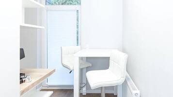 A small, white room with a desk and two chairs, a radiator, and a window with blinds.