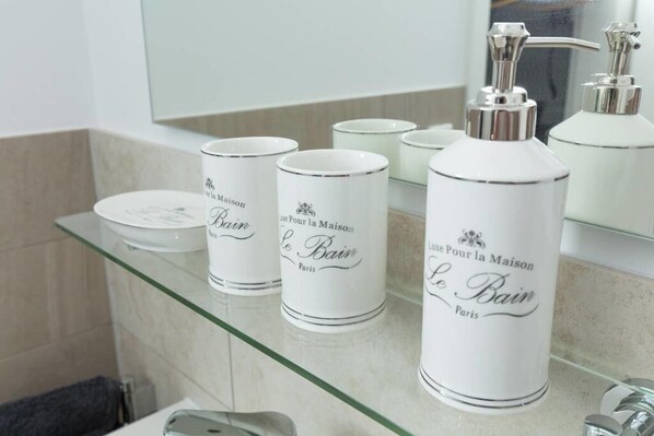 A bathroom with a glass shelf holding white toiletry bottles labeled 'Le Bain Paris'.