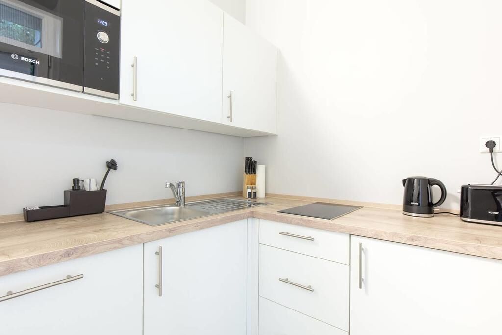 A modern kitchen with white cabinets, a Bosch microwave, a sink, and a kettle.