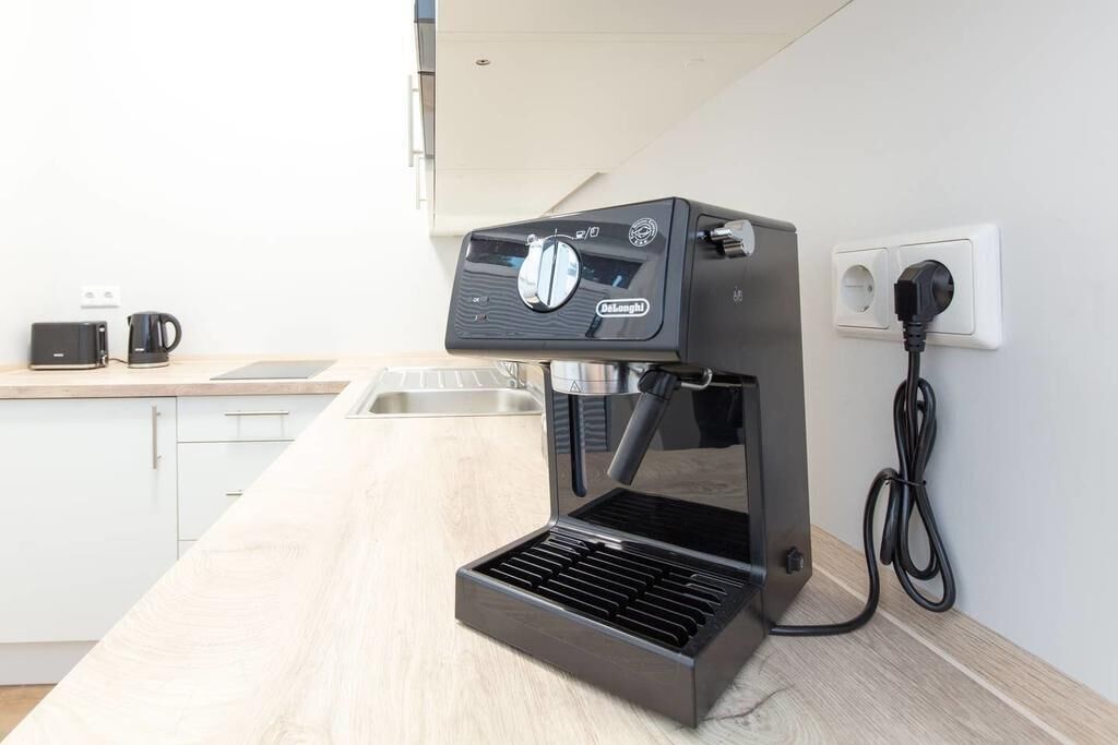 Une machine à café est posée sur un plan de travail de cuisine, à proximité d’une prise électrique, et une cafetière se trouve sur la gauche.