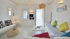 A bright, white room with a sofa, a small table, and a hanging light fixture. - Villa Akoya III by The Pearls Collection (Mykonos)