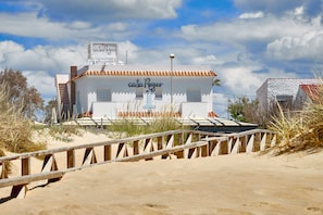 Um edifício com uma placa que diz "casa Reyes" numa praia arenosa, com uma passarela de madeira que leva até ele.