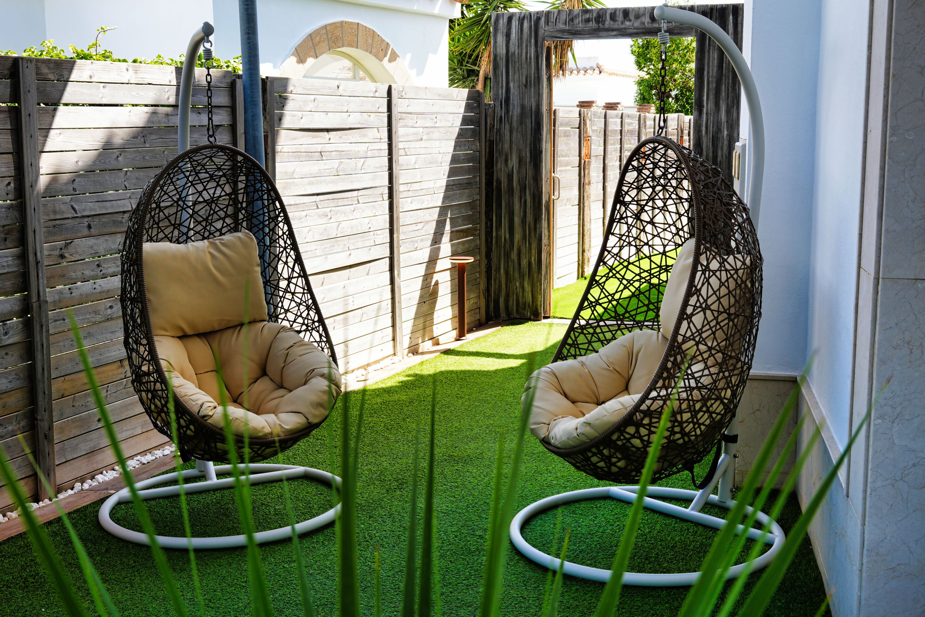 Dos sillones colgantes con cojines, una valla de madera y césped artificial verde.