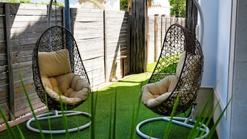 Dos sillones colgantes con cojines, una valla de madera y césped artificial verde.