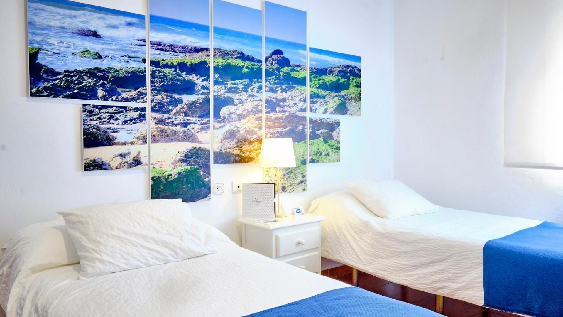 Et hotelværelse med to senge, et natbord og en vægmonteret lampe.