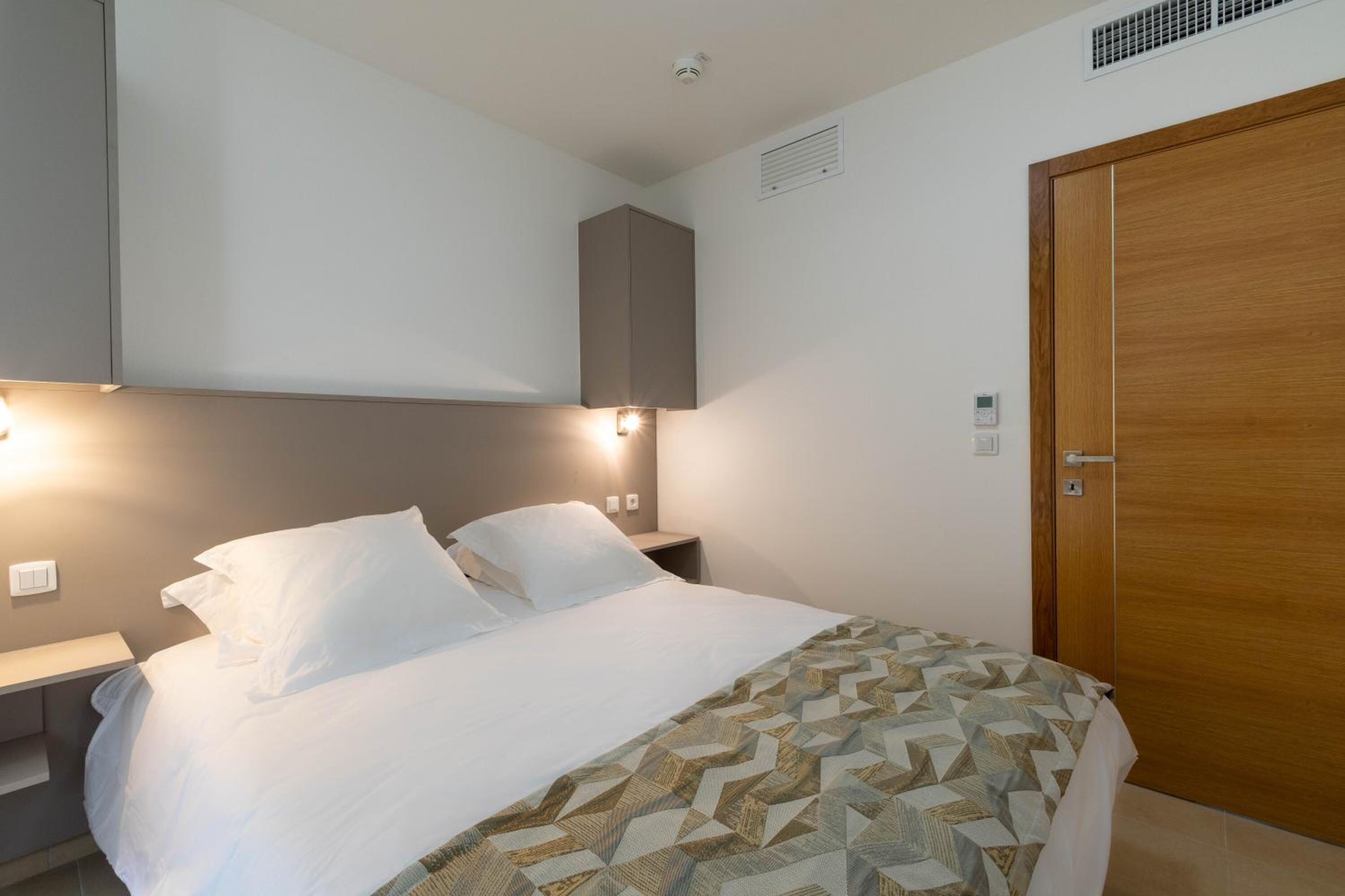Hotellihuone, jossa on sänky, yöpöytä ja vaatekaappi.