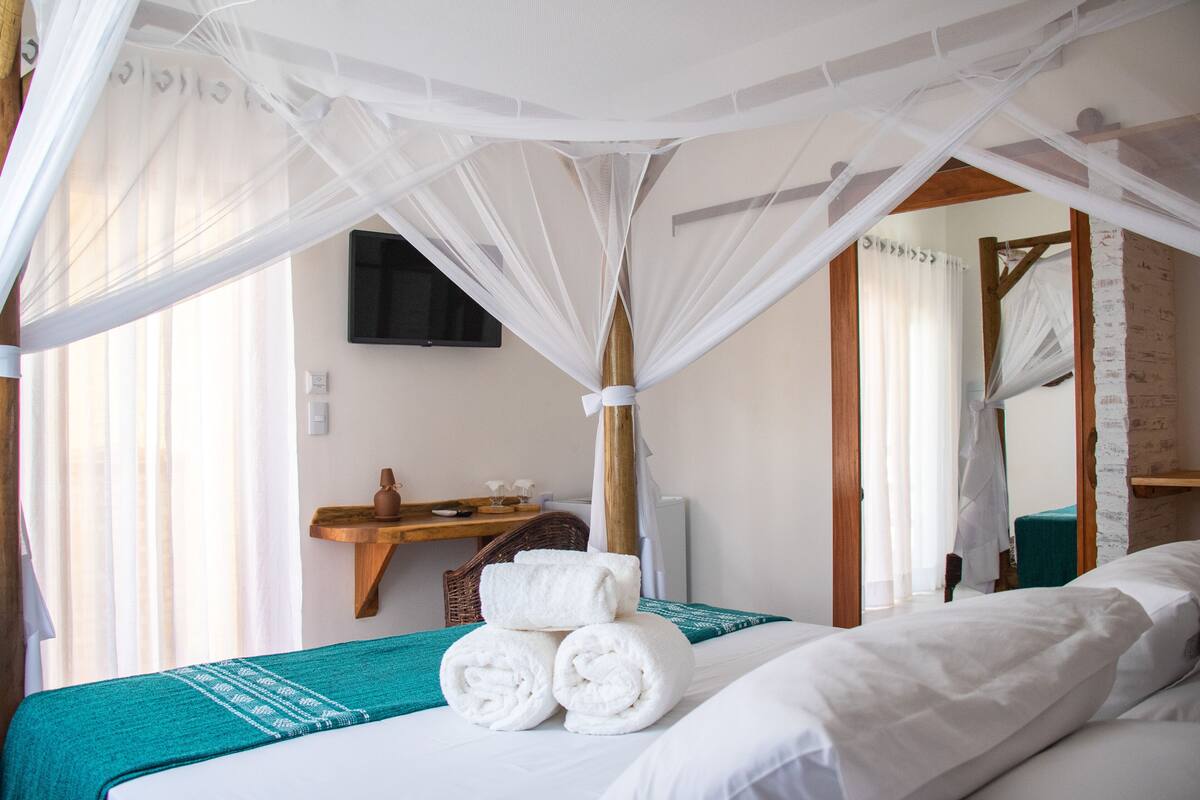 Un dormitorio con cama a dosel, una mesita de noche de madera, un televisor y un espejo.