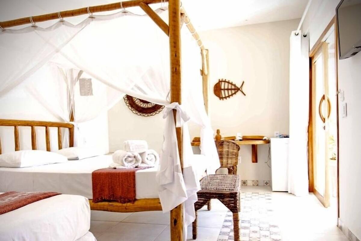 Una habitación con una cama con dosel, una silla, una mesita y un adorno de pared con peces.