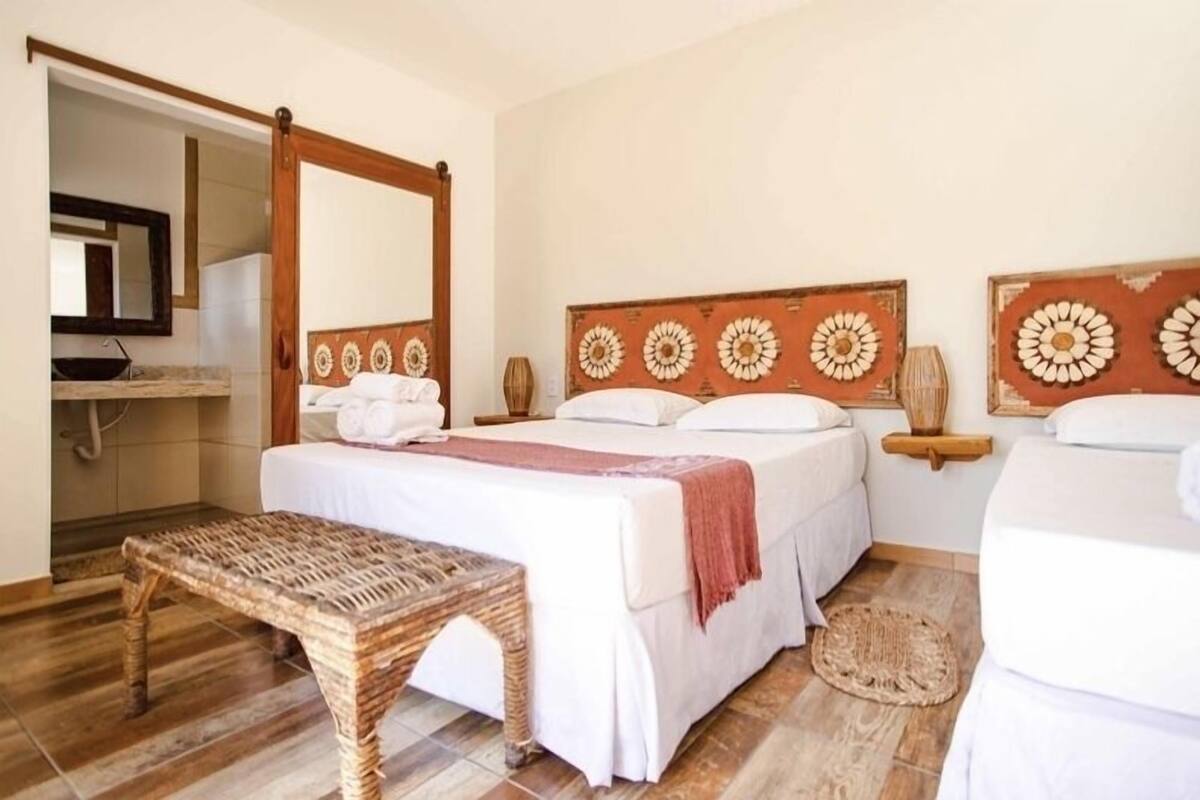 Una habitación de hotel con cama, un banco, un espejo y una pared con diseño floral.