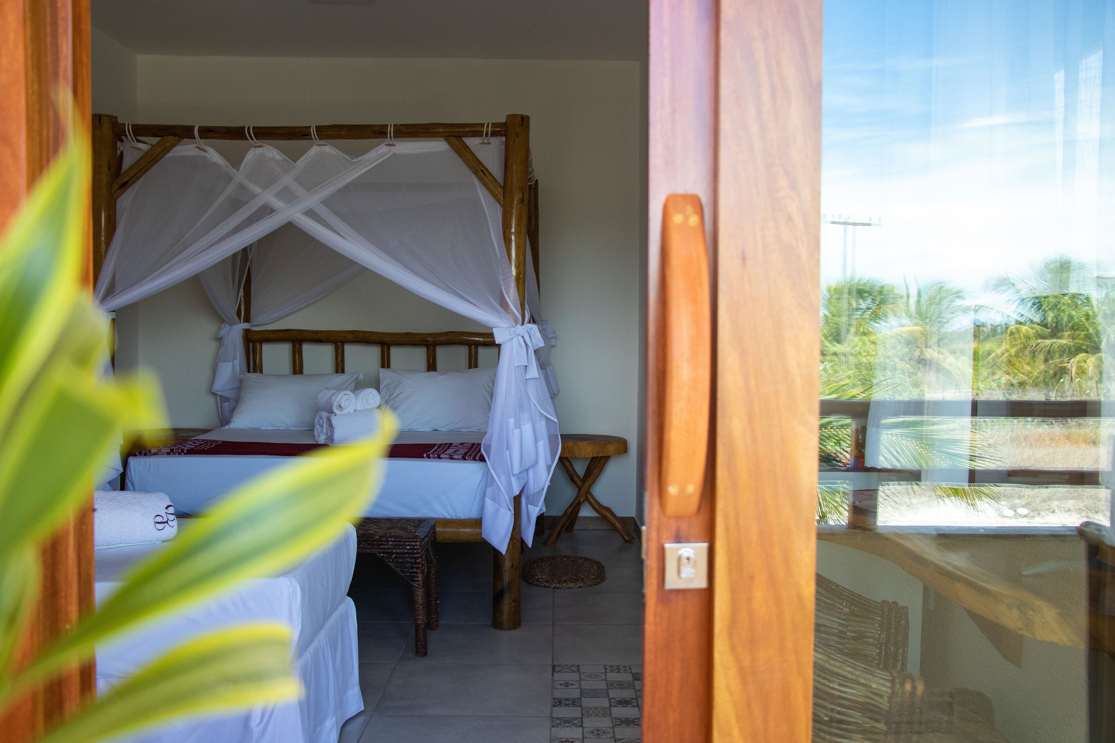 A room with a bed under a wooden canopy, a small table, and a view of the outdoors.
