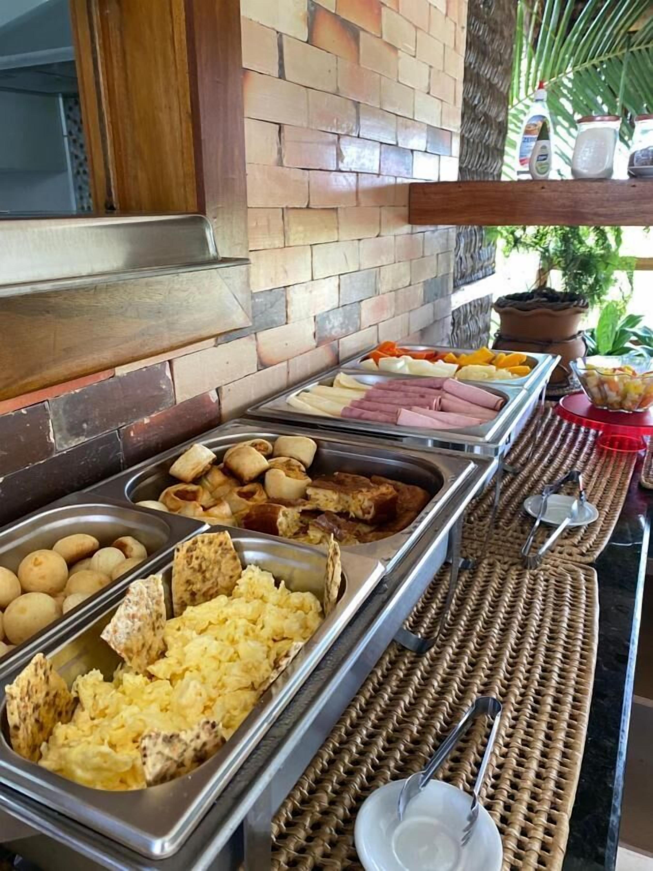 A buffet with various food items including meats, potatoes, and scrambled eggs.
