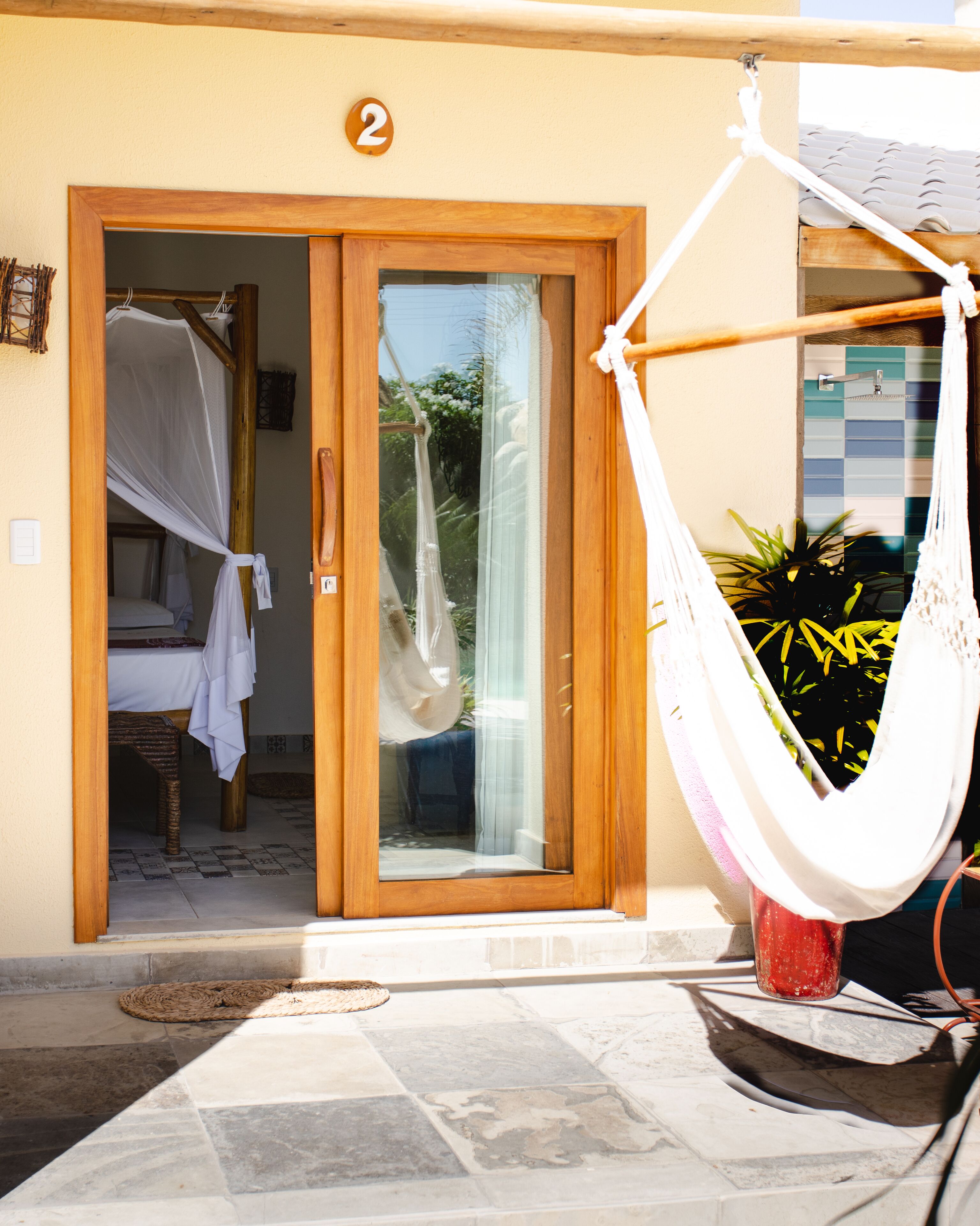 A hotel entrance with a number '2' sign, a wooden door, a glass door, a hammock, and a potted plant.