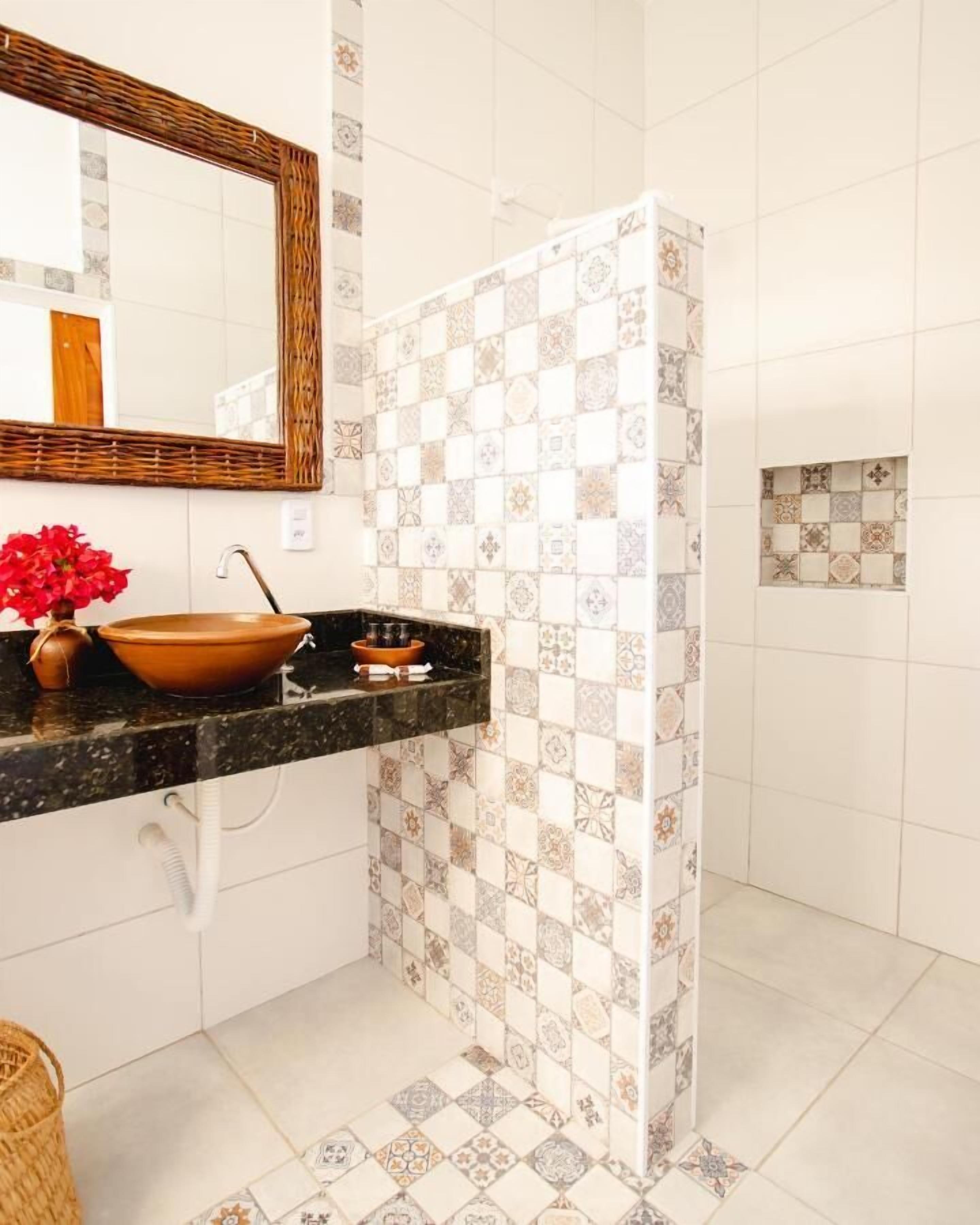 A bathroom with a large mirror, a brown ceramic sink, and patterned tiles on the walls and floor.