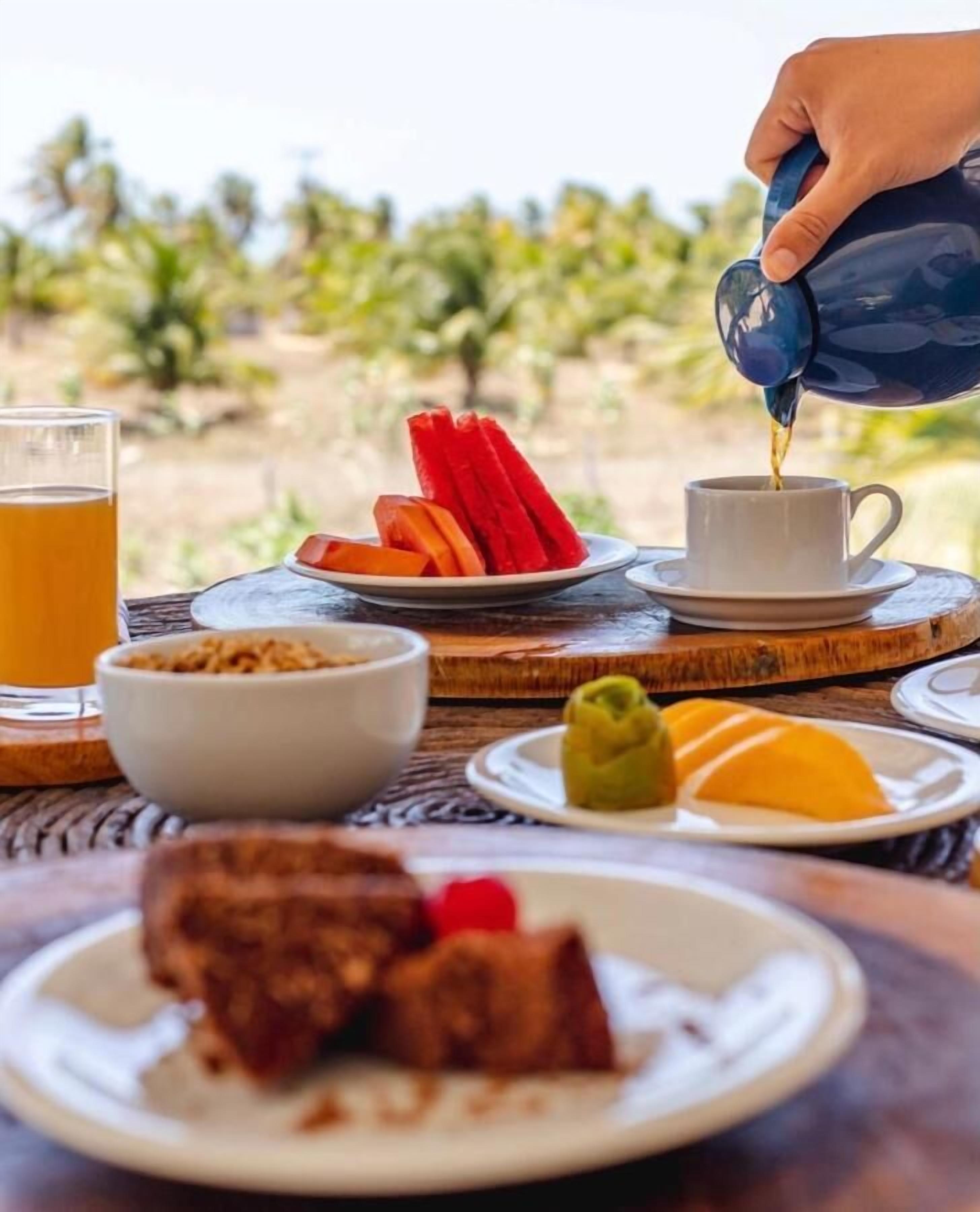 A breakfast setting with a cup of coffee, a glass of orange juice, and plates of food including fruit and a pastry.