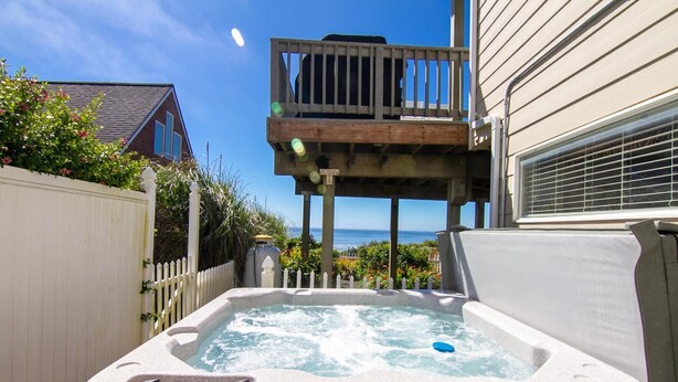 Un jacuzzi en un patio trasero con una terraza de madera y vista al océano.