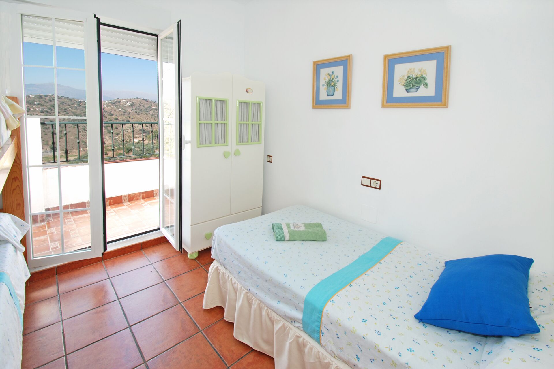 A bedroom with a bed, a balcony, and two framed pictures on the wall.