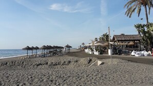 Ein Strand mit strohgedeckten Hütten, Palmen und blauem Himmel.