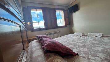 Quarto com cama, janela com vista, radiador e televisão na parede.