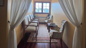 Una habitación con piso de madera, una ventana con cortinas y varias sillas dispuestas alrededor de una mesa.