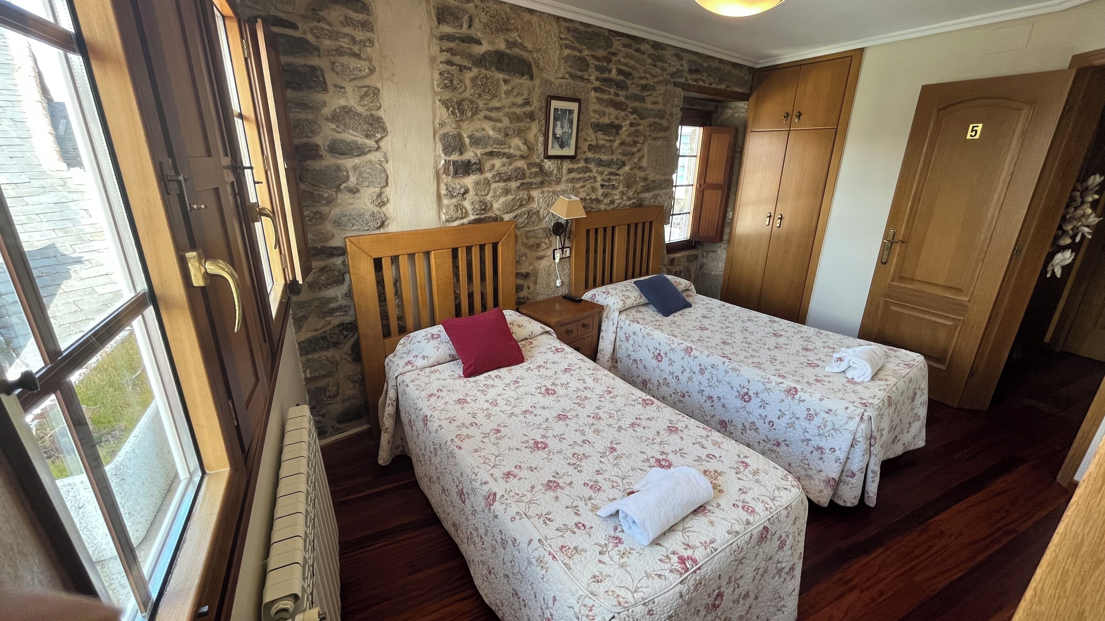 Una habitación con dos camas individuales, una pared de piedra, muebles de madera y una puerta con el número 5.