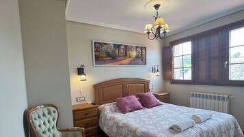 A bedroom with a bed, a chair, a nightstand, a lamp, a painting, and a window.