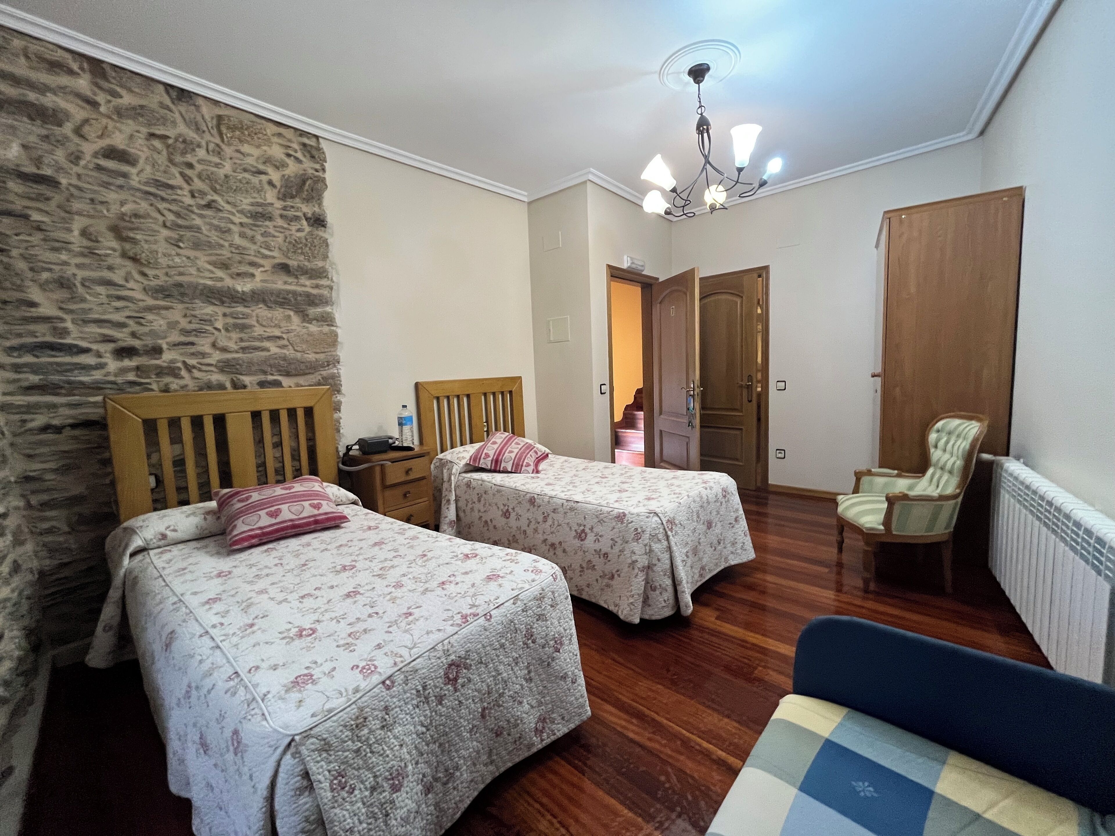 A bedroom with two beds, a stone wall, a wooden door, a chair, and a radiator.