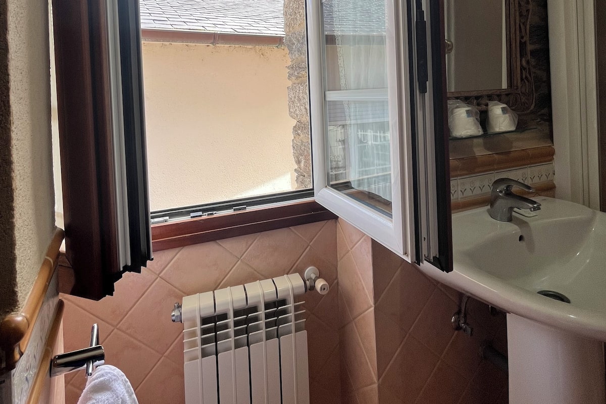 Casa de banho com janela, radiador, pia e toalha pendurada num suporte.