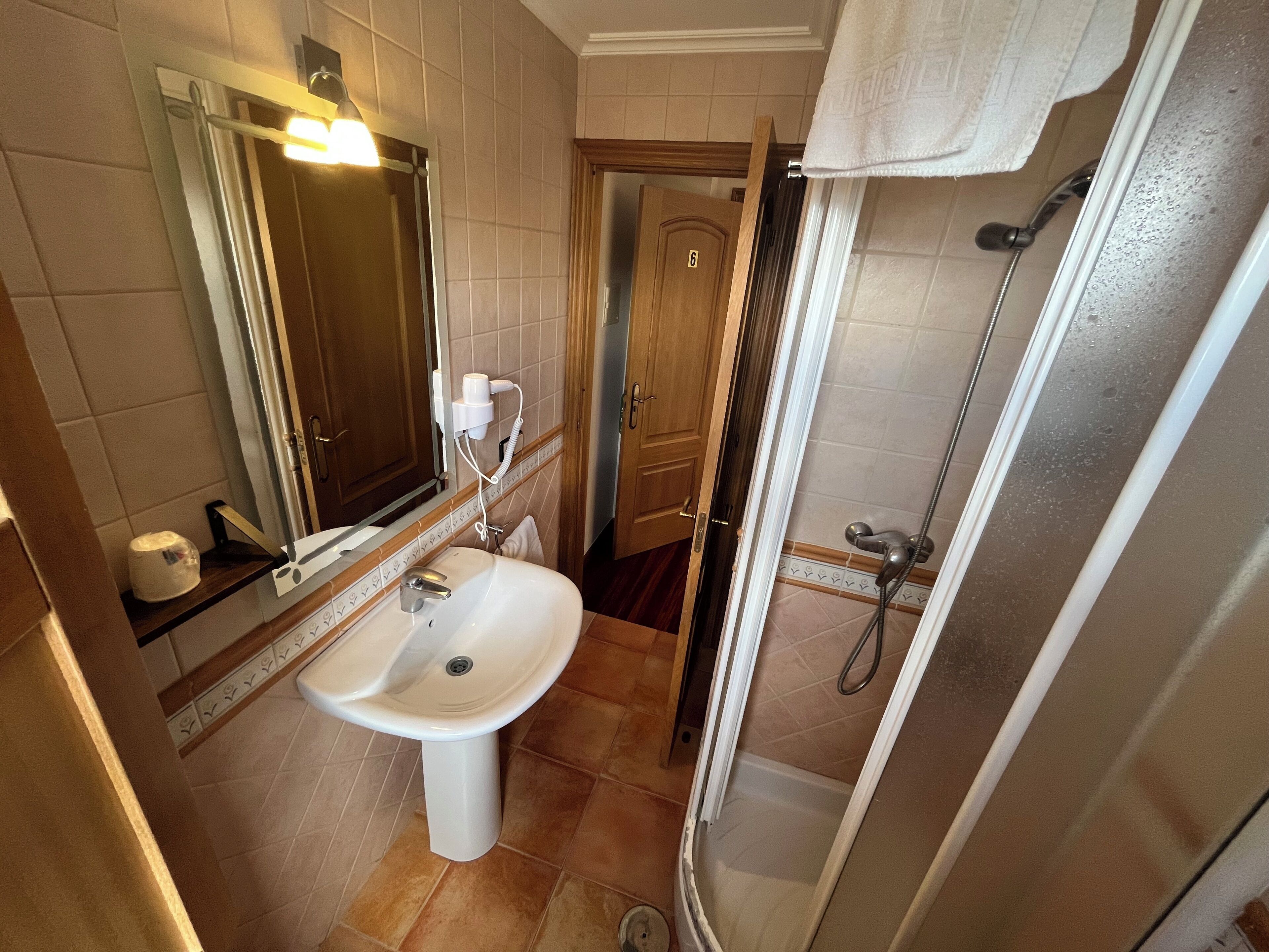 Une salle de bain équipée d’un lavabo, d’un miroir, d’un porte-serviettes, d’une douche et d’une porte portant le numéro 6.