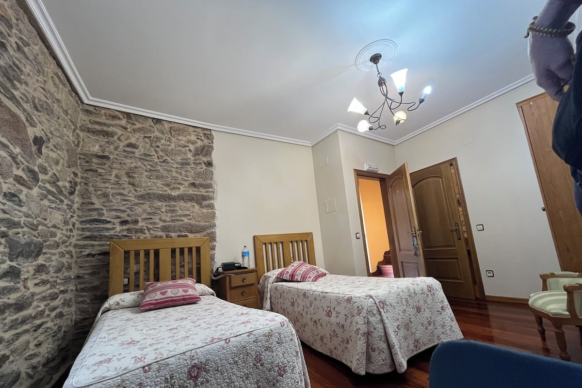 Quarto com duas camas, parede de pedra, porta de madeira e ventilador de teto.