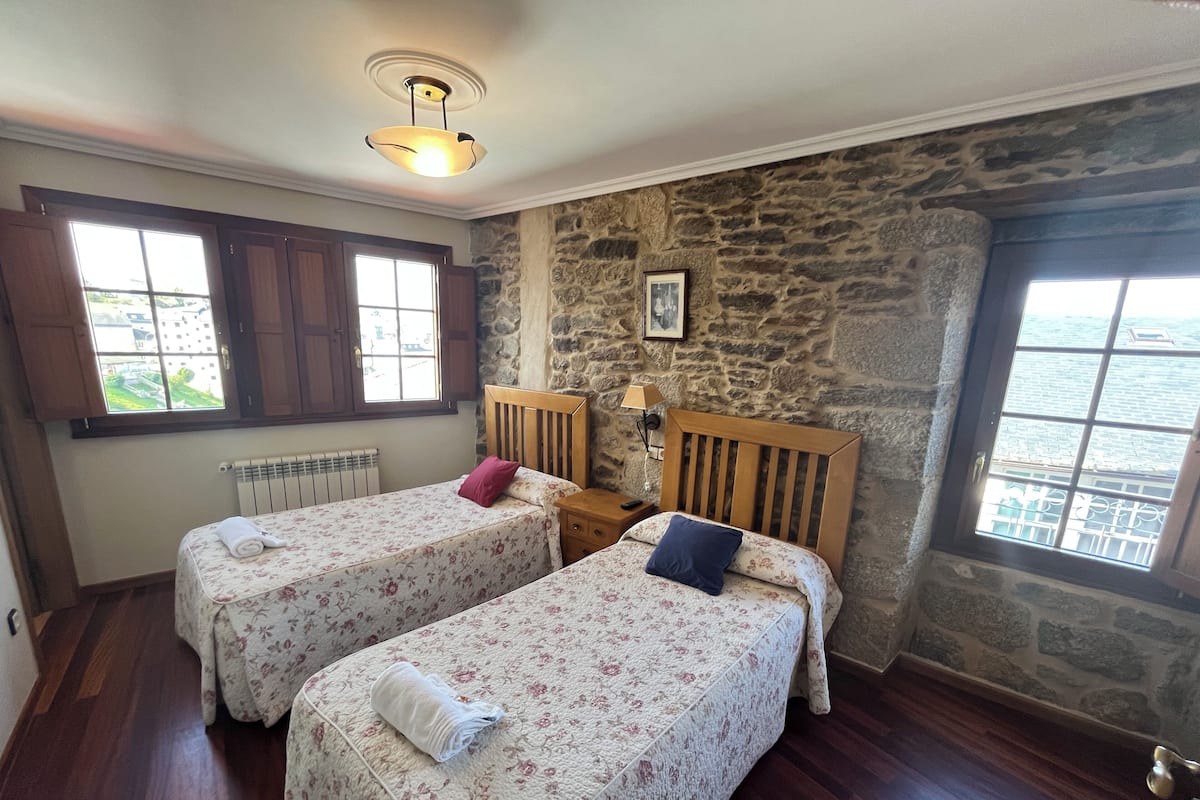 Quarto com duas camas de solteiro, parede de pedra, janela e radiador.
