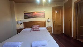 Een netjes opgemaakt bed met een kussen met patroon, een bedlampje en een schilderij van een zonsondergang aan de muur.