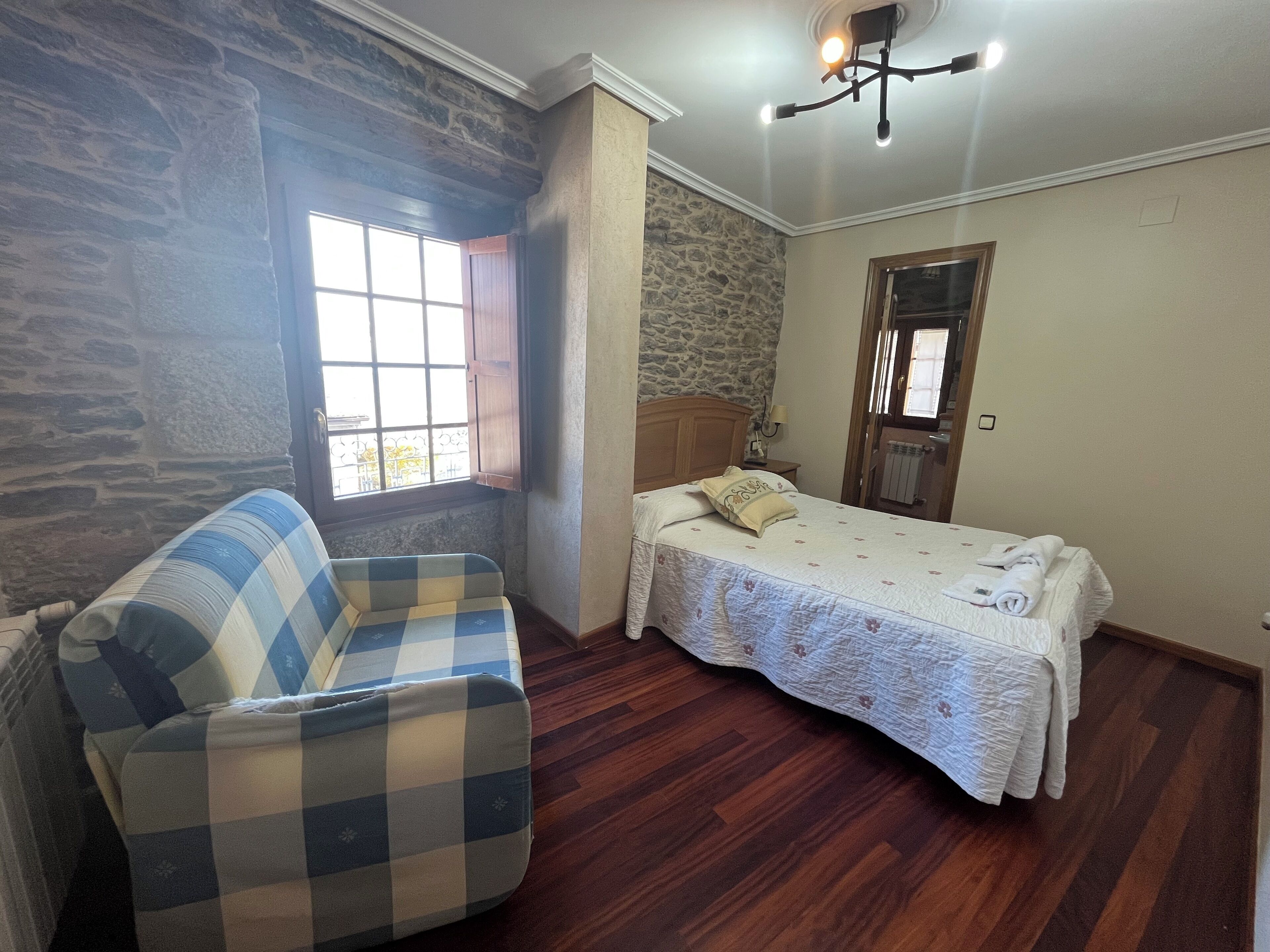 Une chambre avec un canapé à carreaux, un lit recouvert d’une couvre-lit à motifs floraux, un mur en pierre et une porte en bois.
