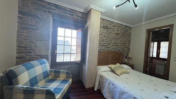 Ein Schlafzimmer mit Steinwand, einem karierten Sofa, einem Bett mit floralem Überwurf und einem Deckenventilator.