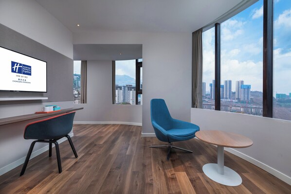 A modern hotel room with a large window, a desk, a blue chair, and a small round table.
