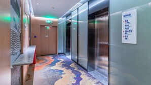 Un corridoio d'hotel con un ascensore, una segnaletica direzionale e una moquette decorata.