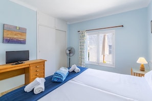 Une chambre d’hôtel avec un lit, un bureau avec une télévision, un ventilateur et une fenêtre avec des rideaux.