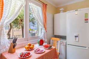 Une cuisine avec une table mise pour le repas, un réfrigérateur et une fenêtre avec des rideaux.