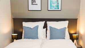 A neatly made bed with white and blue pillows, two bedside lamps, and two framed pictures on the wall. - BENSIMON apartments Charlottenburg (Berlin)