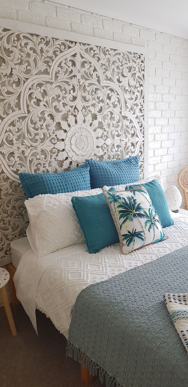 A bed with a white and blue patterned headboard, a teal throw blanket, and multiple pillows.