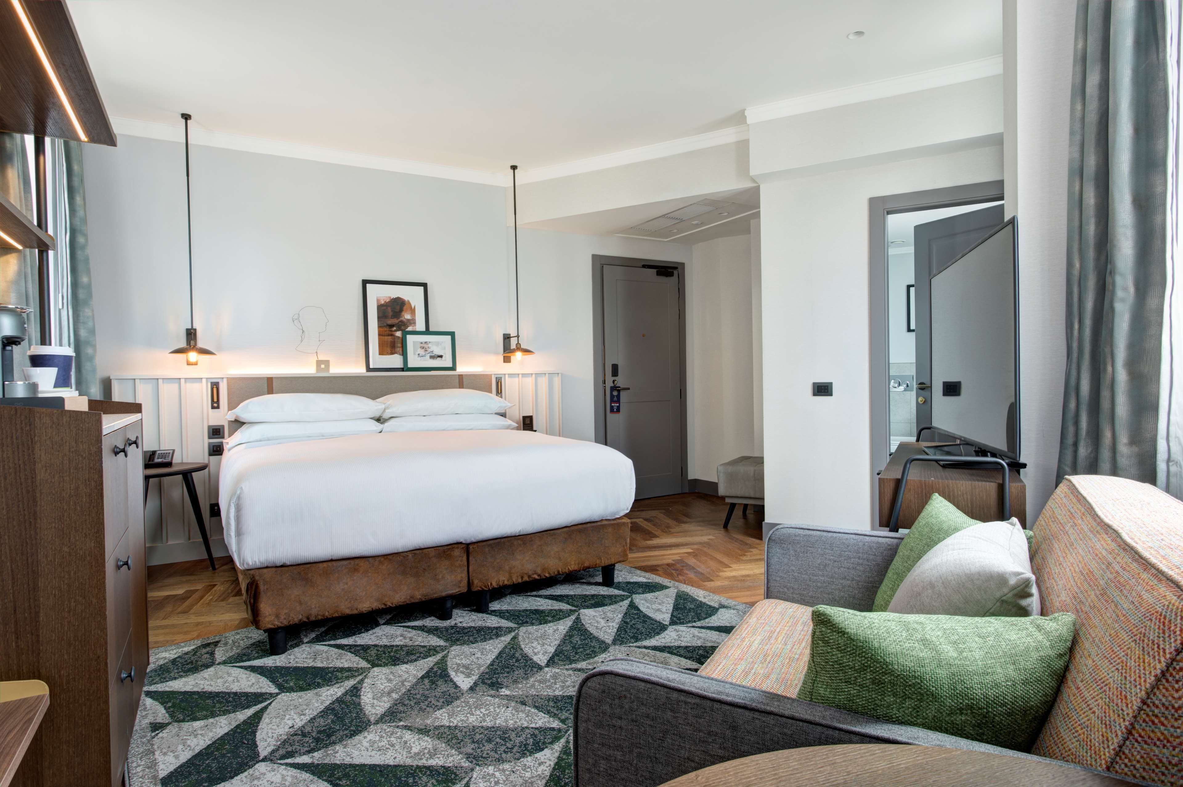 Een moderne hotelkamer met een groot bed, een bank, een bureau en een spiegel.