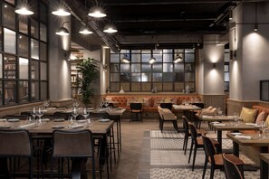 A restaurant with multiple dining tables, chairs, and a central seating area with a sofa and cushions. - DoubleTree by Hilton Rome Monti (Rome)